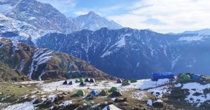 Cluster of colorful tents set up on a snow-dusted mountain ridge in Triund with dramatic views of the Dhauladhar range