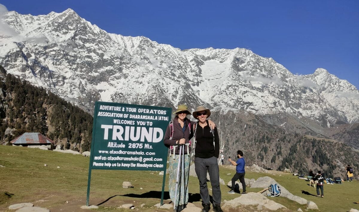 two people standing in front of a sign with snow covered mountains in the background