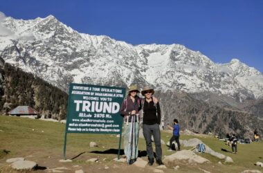 two people standing in front of a sign with snow covered mountains in the background