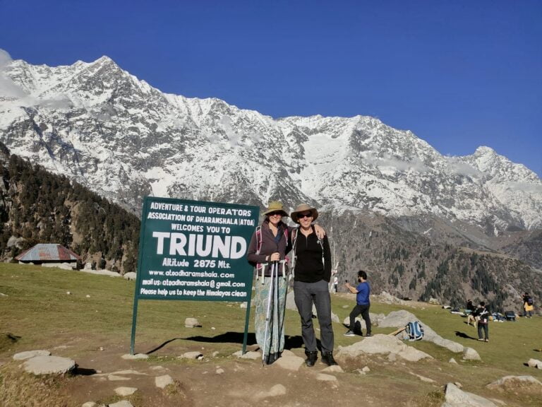 two people standing in front of a sign with snow covered mountains in the background