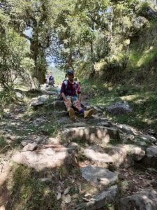 Trekker sitting on a rocky forest trail surrounded by pine and deodar trees in Dharamsala