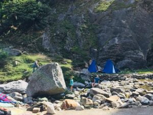 Campers exploring boulders near tents at a riverside campsite in the Himalayas