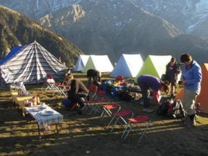 “Campers setting up tents and relaxing at Triund campsite with mountain views in the background.”