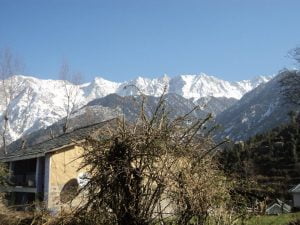 “Traditional house in Naddi village with snow-covered Dhauladhar mountains in the background.”