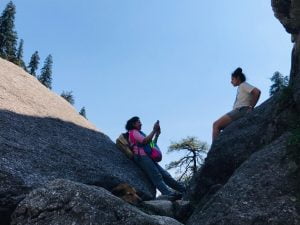 Two women resting on boulders during a Himalayan trek near Dharamsala, Himachal Pradesh