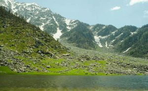 Scenic view of Kareri Lake with snow-capped Dhauladhar mountains and green meadows
