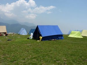 Colorful trekking tents set up on a grassy ridge in the Himalayas under a bright sky