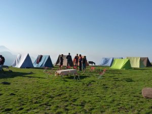 Colorful tents set up at a high-altitude campsite in Himachal with trekkers enjoying the morning view