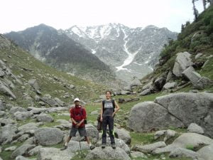 Trekkers on Kareri Lake trail surrounded by rocky terrain and snow-covered peaks in Himachal Pradesh