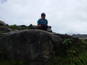 Trekker sitting on a large rock surrounded by greenery on a cloudy day in the hills near Dharamshala