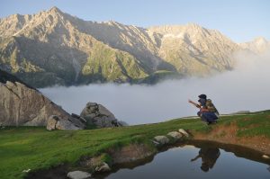 Trekker resting beside an alpine lake with Dhauladhar mountains in the background
