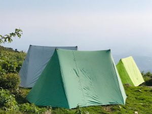 Colorful trekking tents pitched on a green hillside in Dharamshala