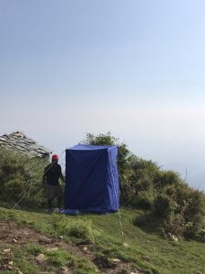Portable toilet tent set up on a grassy hillside during a Himalayan trek in Dharamshala