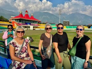 Group of tourists posing at Dharamsala Cricket Stadium with Dhauladhar mountains in the background
