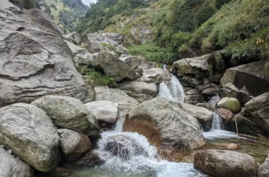 Hikers resting near Gallu Waterfall on a forest trail above Dharamkot