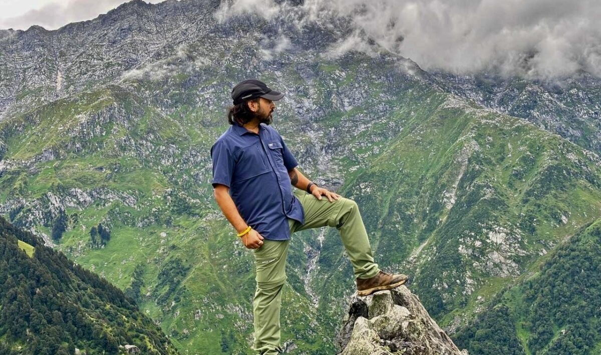 Trekker standing on a rock overlooking the lush green Dhauladhar mountains near Dharamshala