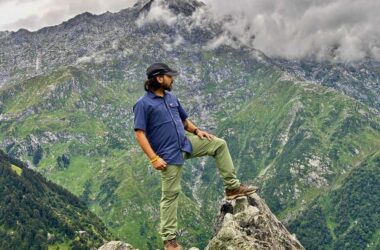 Trekker standing on a rock overlooking the lush green Dhauladhar mountains near Dharamshala