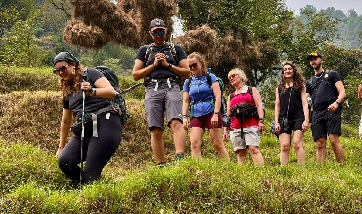 Group of trekkers walking through lush green fields in Himachal Pradesh with pine trees and hills in the background