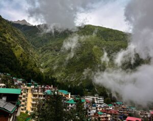 Scenic view of Mcleodganj town with colorful buildings, surrounded by misty green mountains in Dharamsala, Himachal Pradesh.